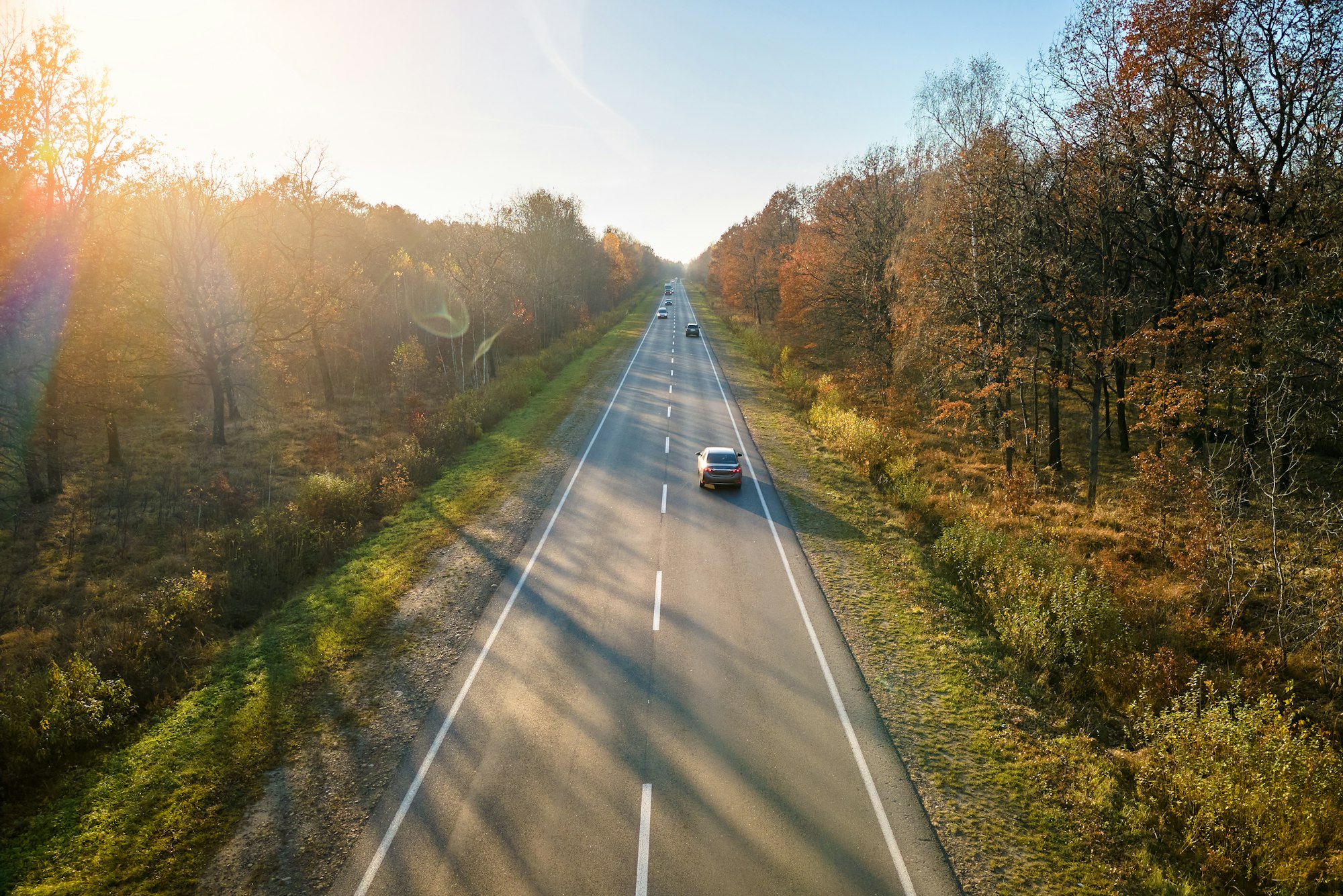 Aerial view of intercity road with fast driving cars between autumn forest trees at sunset.