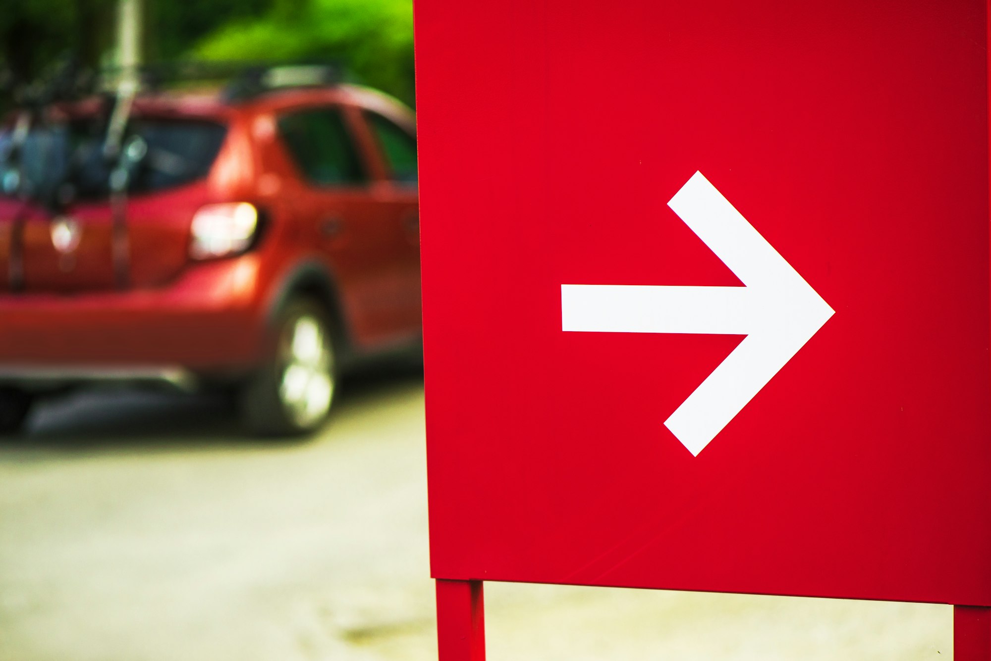 Direction arrow sign with car in background