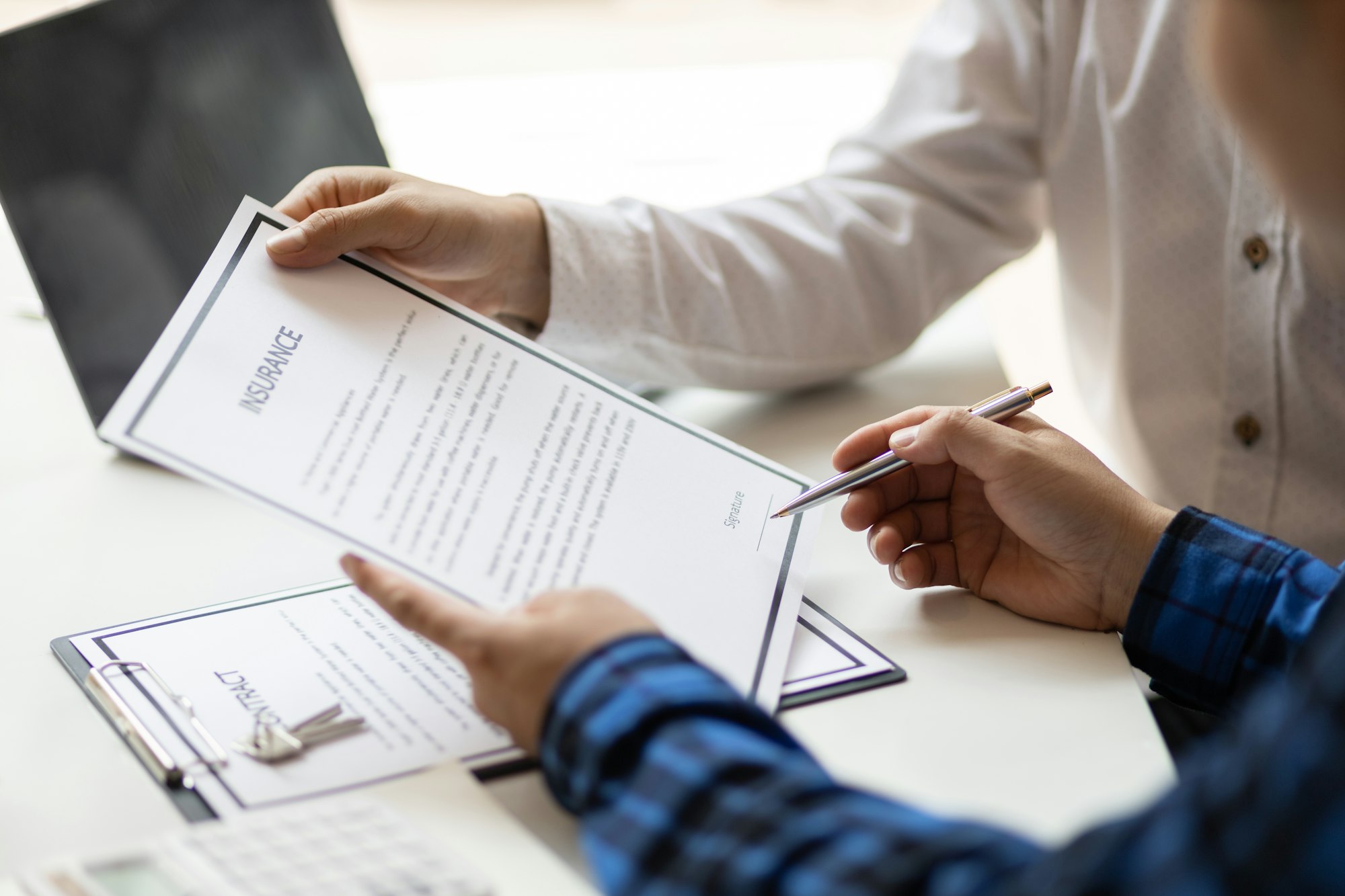 Man in office showing an insurance policy and pointing with a pen where the policyholder must to sig